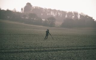 Mann beim Sondeln mit Metalldetektor auf dem Acker